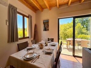 A dining area with a table set for four, a painting on the wall, and a view of greenery through the glass door. - Beautiful house in a holiday park with a pool (Lacapelle Marival)