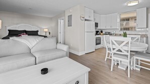 Eine moderne, hell eingerichtete Wohnung mit Wohnbereich, ausgestattet mit einem weißen Sofa, einem Esstisch mit Stühlen und einer Küche mit weißen Schränken und Geräten.