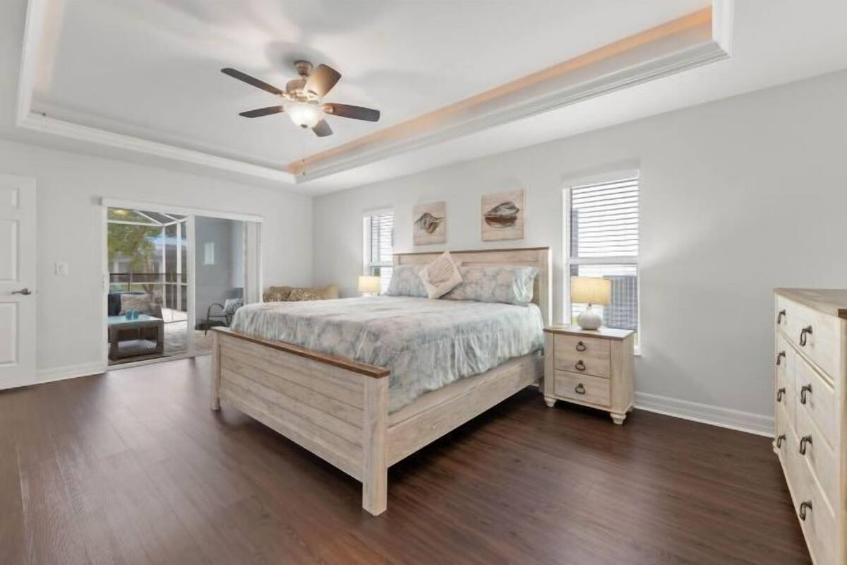 A bedroom with a wooden bed, a ceiling fan, a nightstand, a dresser, and a window with blinds.