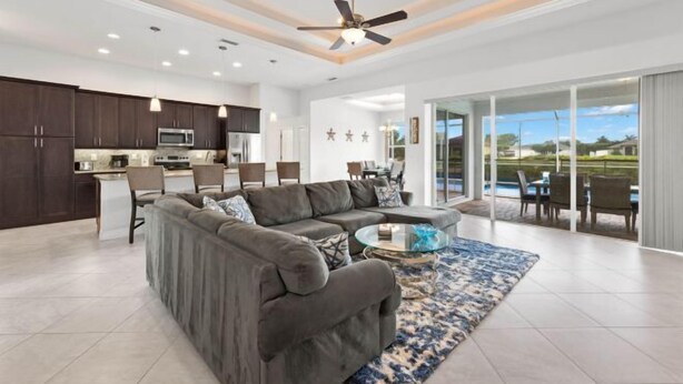 A spacious living room with a gray sectional sofa, a glass coffee table, and a blue patterned rug. - Villa Rosa (Cape Coral)