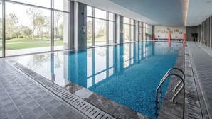A large indoor swimming pool with clear glass walls, a tiled floor, and a view of a green landscape. - LEBANSHAN HOTELS HEFEI (Hefei)