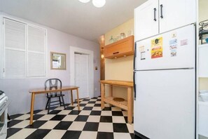 A compact kitchen with a checkered floor, a refrigerator with magnets, a small wooden table, and a chair. - Charming 3-Bedroom Apartment in Midtown West (New York)