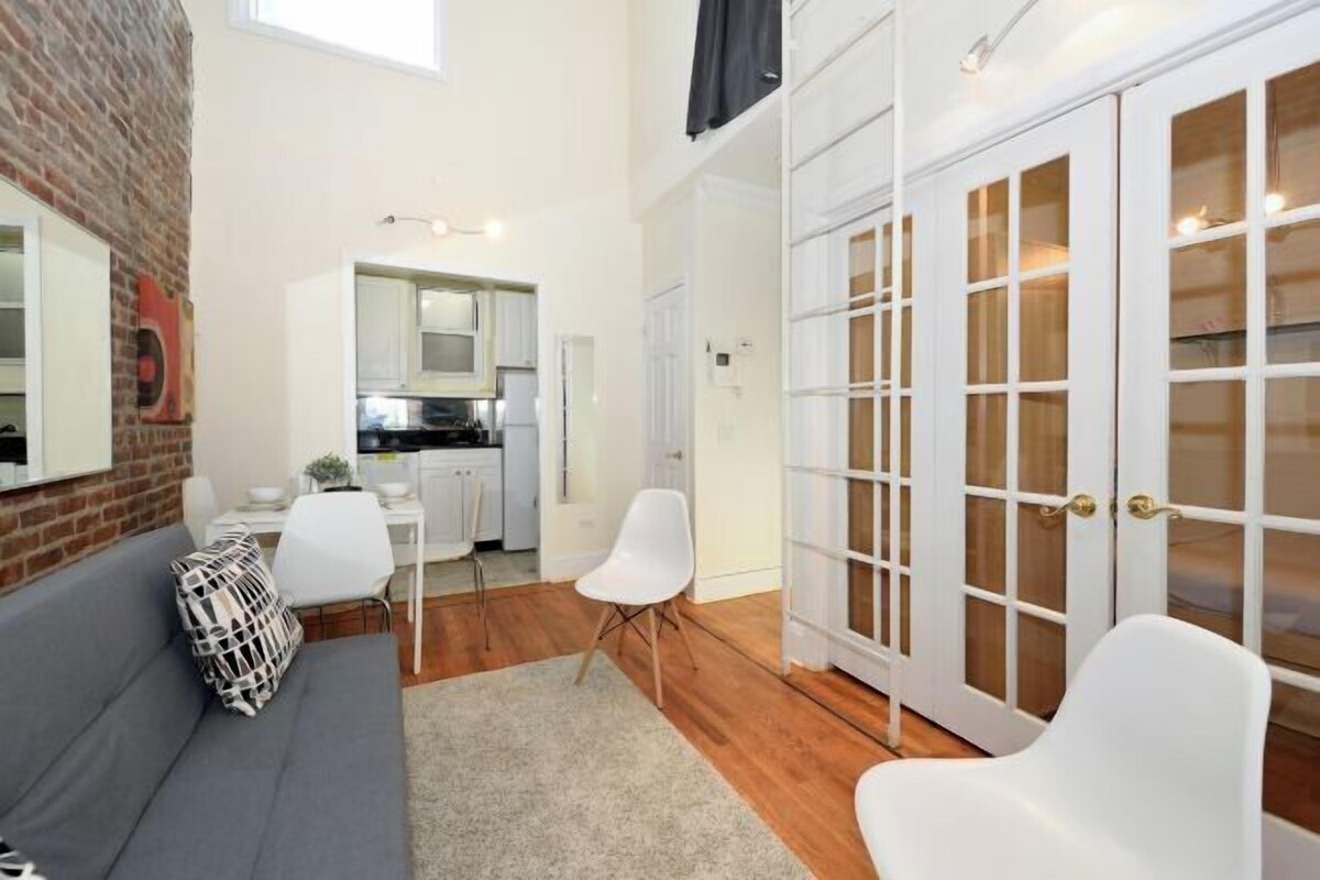 A modern apartment with a grey sofa, white chairs, a kitchen area, and a large sliding glass door closet.
