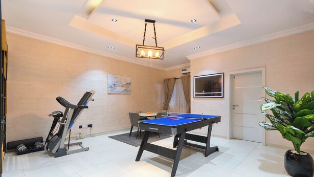 Una habitación con mesa de ping pong, equipo de ejercicio, una planta en maceta y una puerta.