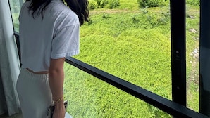 Eine Person steht an einem großen Fenster mit Blick auf eine grüne Landschaft.