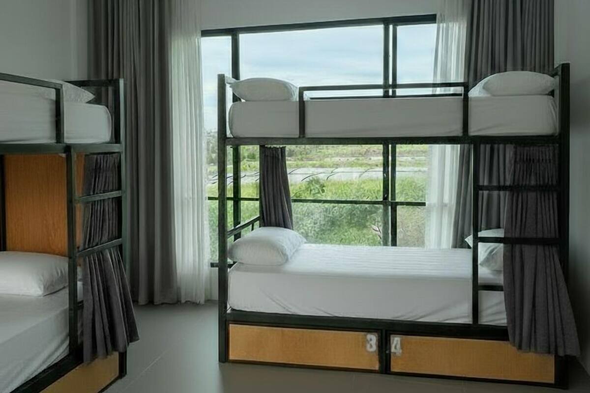 A room with bunk beds, a large window, and curtains.