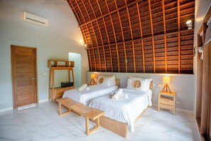 A bedroom with two beds, wooden headboard, bedside tables with lamps, a wooden bench, and a large mirror. - Kayu Jati Cottages (Penida Island)