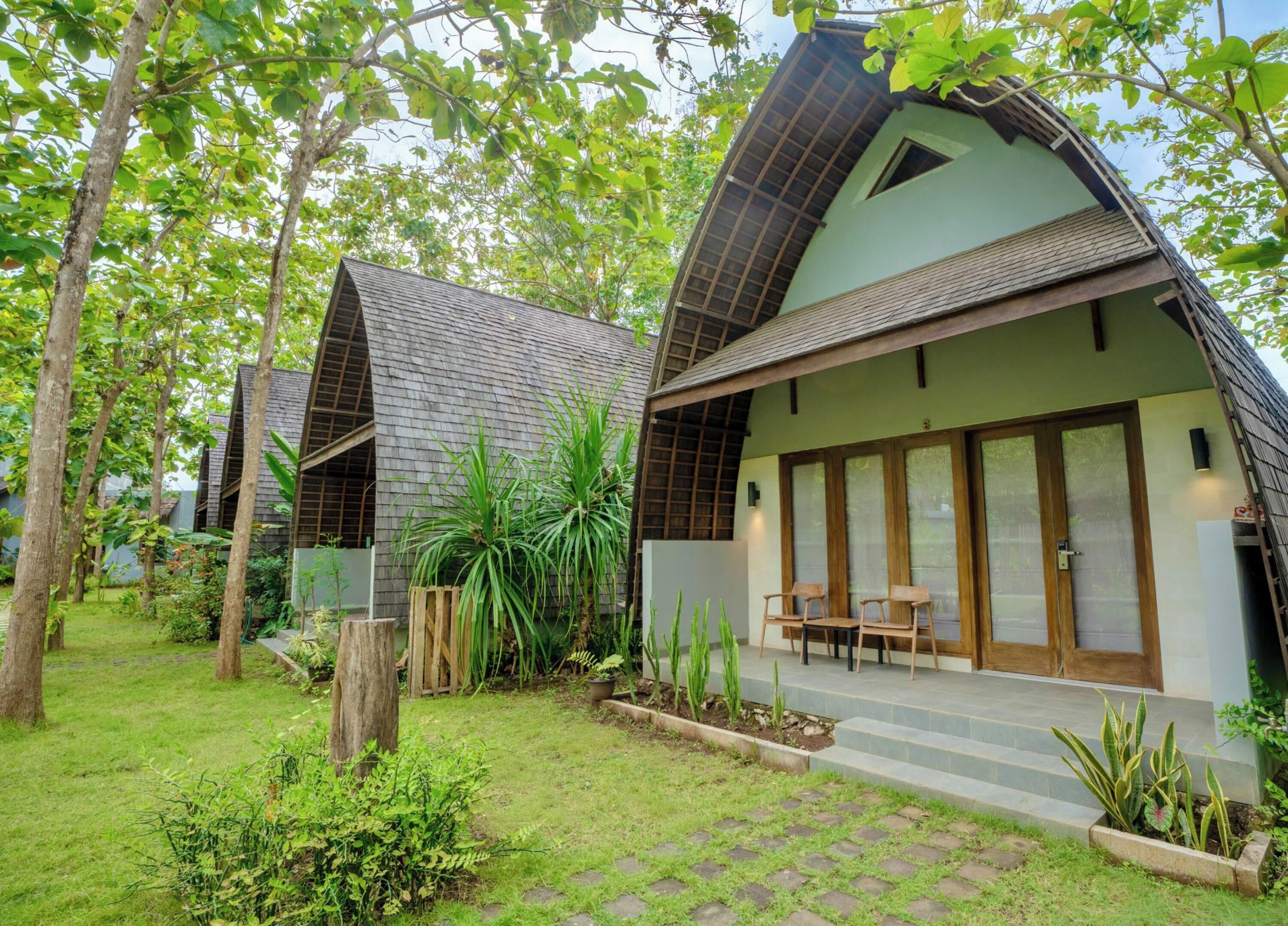 A modern house with a sloped roof, a porch with wooden chairs, and a garden with various plants.