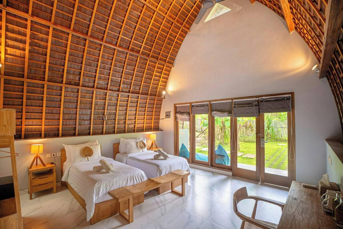 Ein geräumiges Zimmer mit zwei Betten, Holzboden und großen Schiebeglasüren zum Garten.