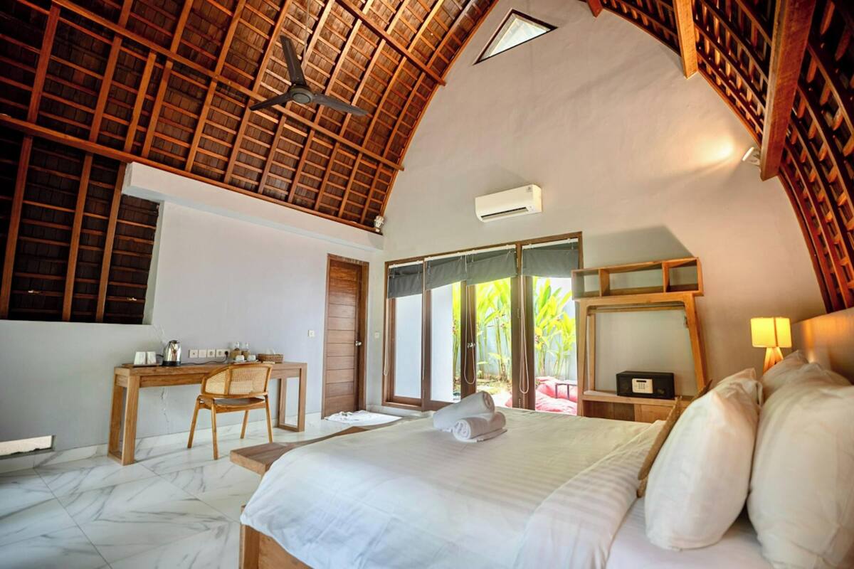 Ein Schlafzimmer mit einem großen Bett, einem Schreibtisch und einem Stuhl. Es gibt einen Deckenventilator, ein Fenster und eine Tür, die nach draußen führt.
