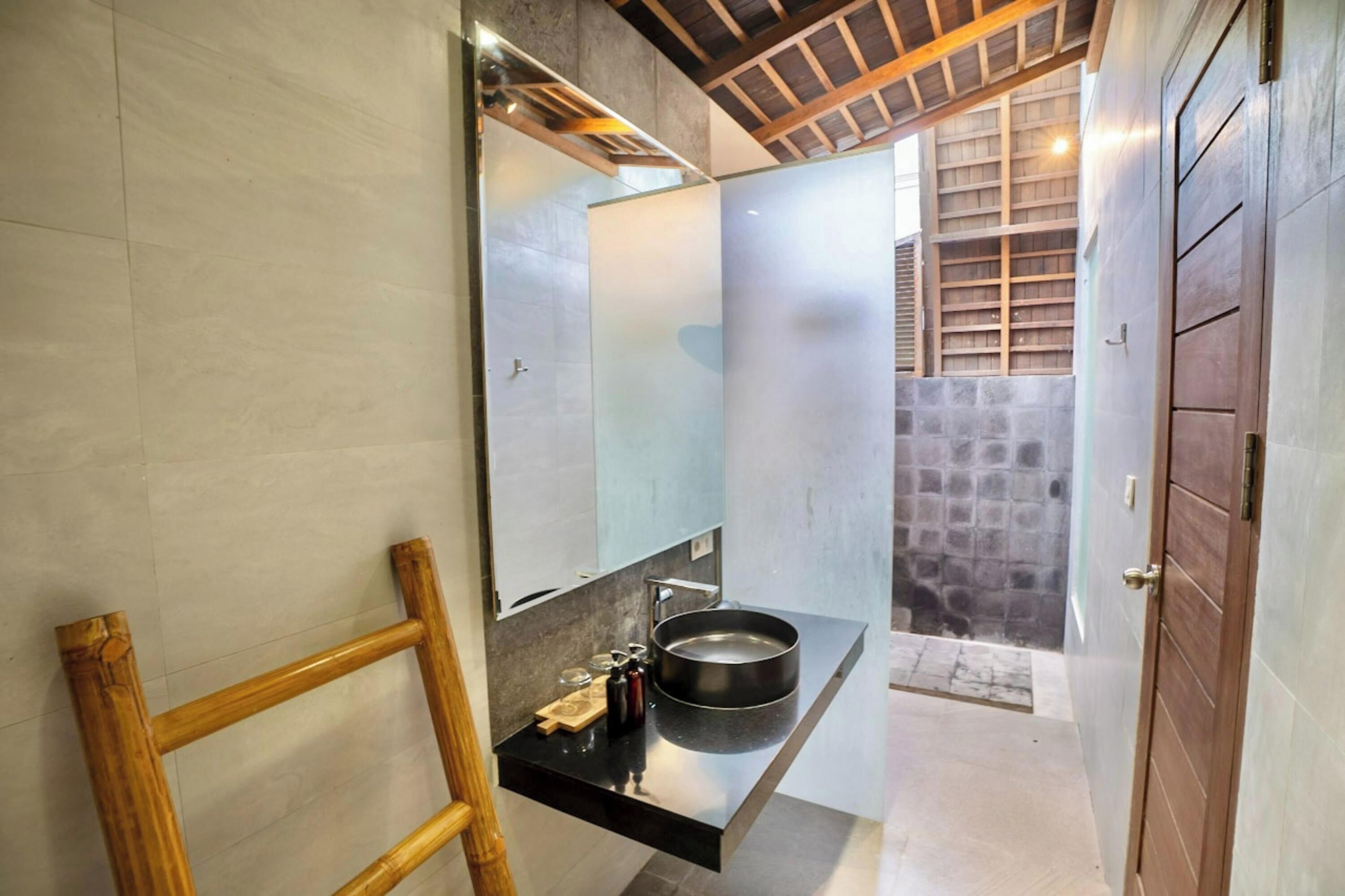 A modern bathroom with a black sink, a mirror, and a wooden ladder.