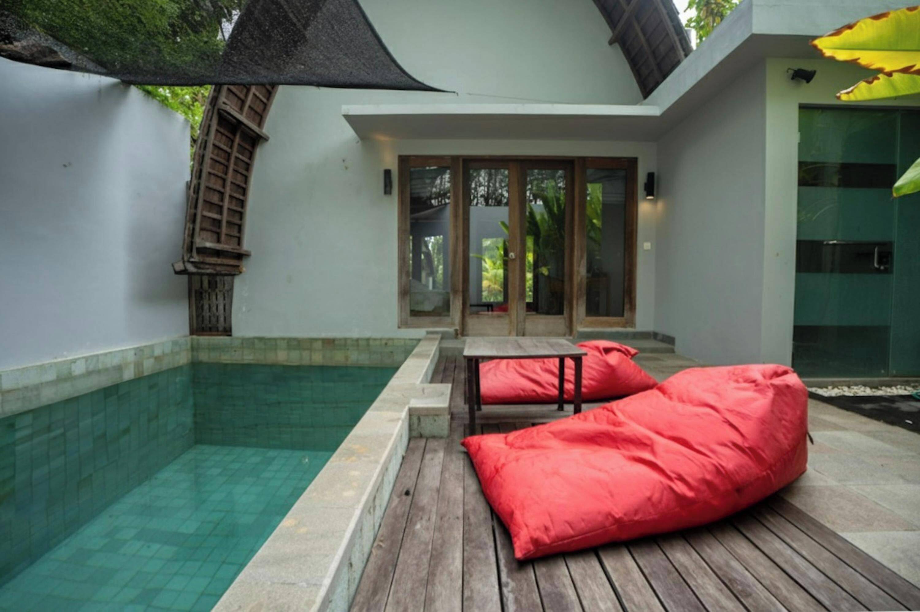 A poolside area with a wooden deck, a glass door entrance, and a red bean bag chair.