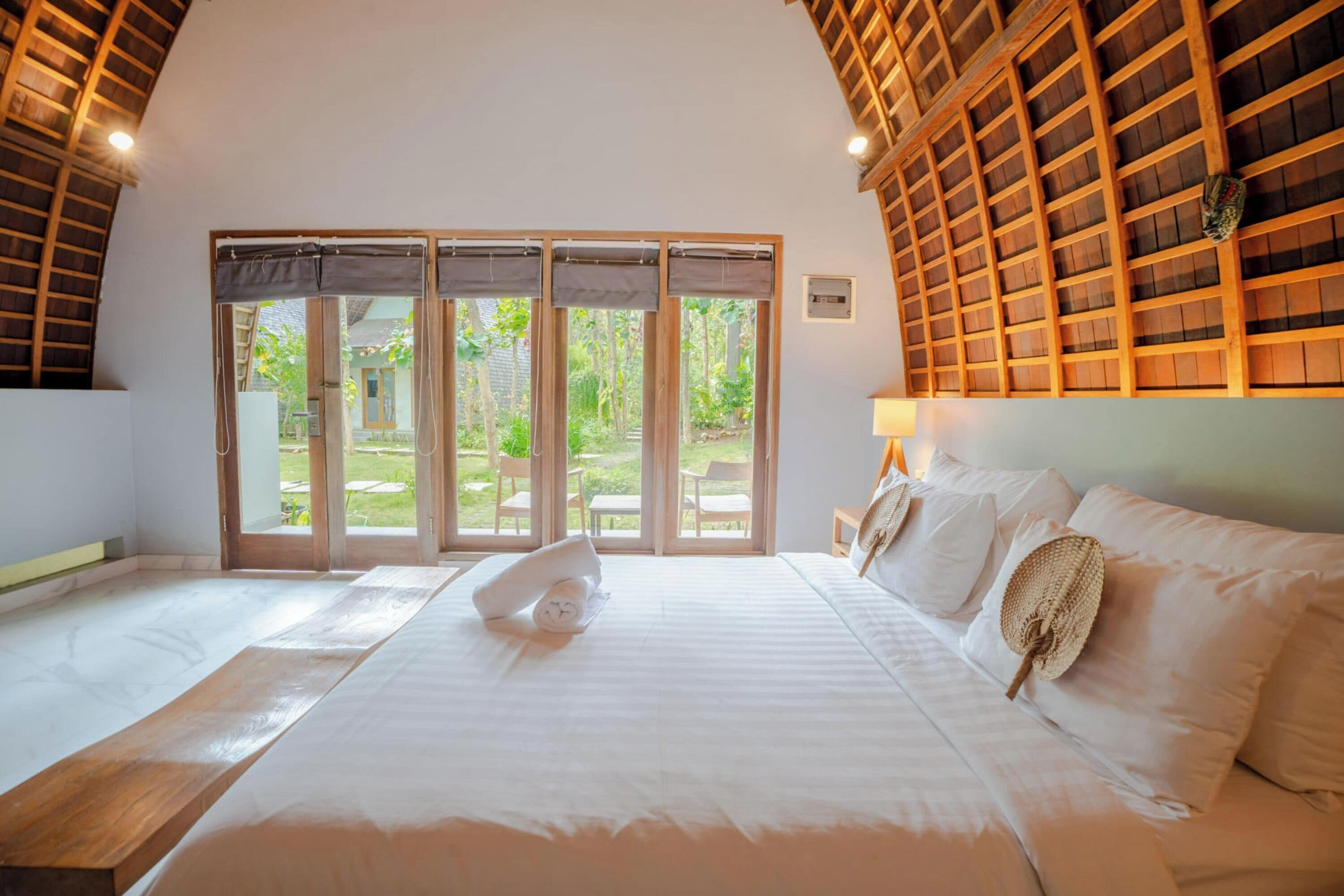 A bedroom with a large bed, a wooden ceiling, and a view of the outdoors through a glass door.