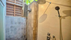 A shower area with a handheld showerhead, a wall-mounted control panel, and a tiled wall. - Kayu Jati Cottages (Penida Island)