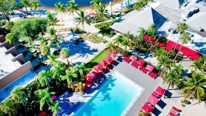 An aerial view of a resort with a swimming pool, palm trees, and beach access. - PgaVillageResort by AmericanVacationLiving 1 Br (Port St. Lucie)