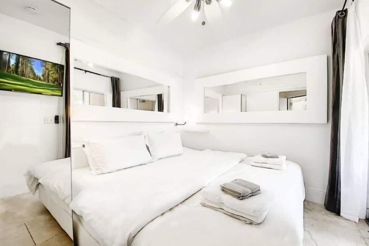 Ein modernes Schlafzimmer mit einem großen Bett, zwei Wandspiegeln und einem Deckenventilator.