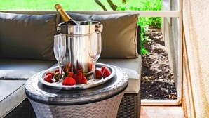 A wicker chair with a cushioned seat, a metal ice bucket with a champagne bottle, and a tray with strawberries. - PgaVillageResort by AmericanVacationLiving 1 Br (Port St. Lucie)