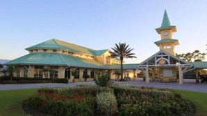 A large building with a green roof and a clock tower, surrounded by landscaped gardens. - PgaVillageResort by AmericanVacationLiving 1 Br (Port St. Lucie)