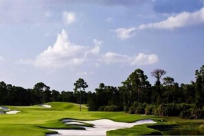 A golf course with sand bunkers, a water hazard, and a clear sky. - PgaVillageResort by AmericanVacationLiving 1 Br (Port St. Lucie)