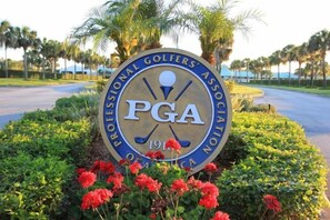 A PGA logo surrounded by greenery and flowers. - PgaVillageResort by AmericanVacationLiving 1 Br (Port St. Lucie)