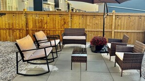 Un patio al aire libre con muebles de mimbre, un paraguas grande y una valla de madera.