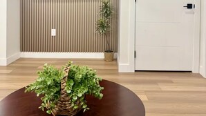 Una sala de estar moderna con un televisor de pantalla plana montado en una pared de madera, una planta en maceta y una mesa redonda de madera con una cesta tejida.