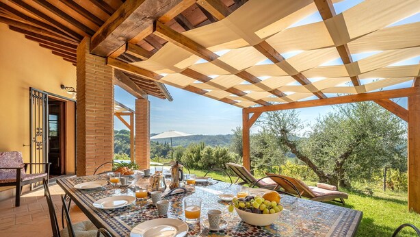 Un área de comedor al aire libre con una mesa y sillas de cerámica, y vista al campo.