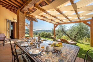 Zona pranzo all'aperto con tavolo e sedie in piastrelle, vista sulla campagna.