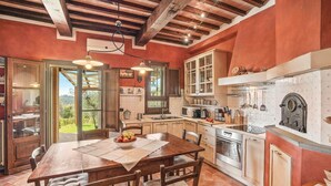 Una cocina rústica con vigas de madera, una mesa de comedor con sillas y vistas al jardín a través de un ventanal abierto.