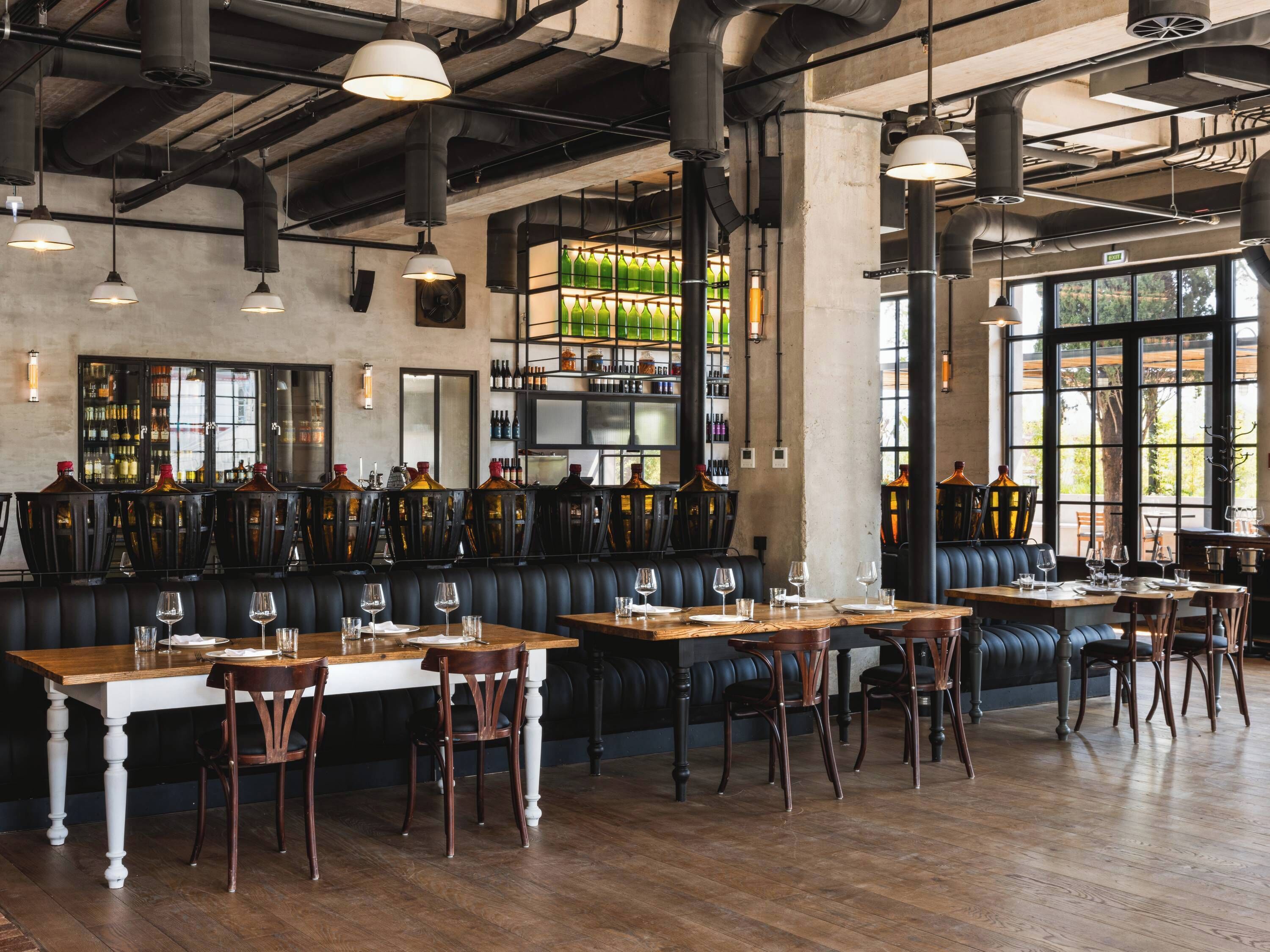 A restaurant with wooden tables, black leather booths, and a bar area with bottles.