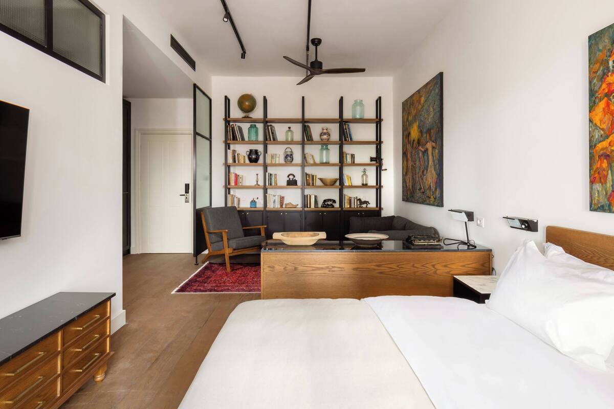 Une chambre moderne avec un grand lit, un bureau en bois, une bibliothèque et un ventilateur de plafond.