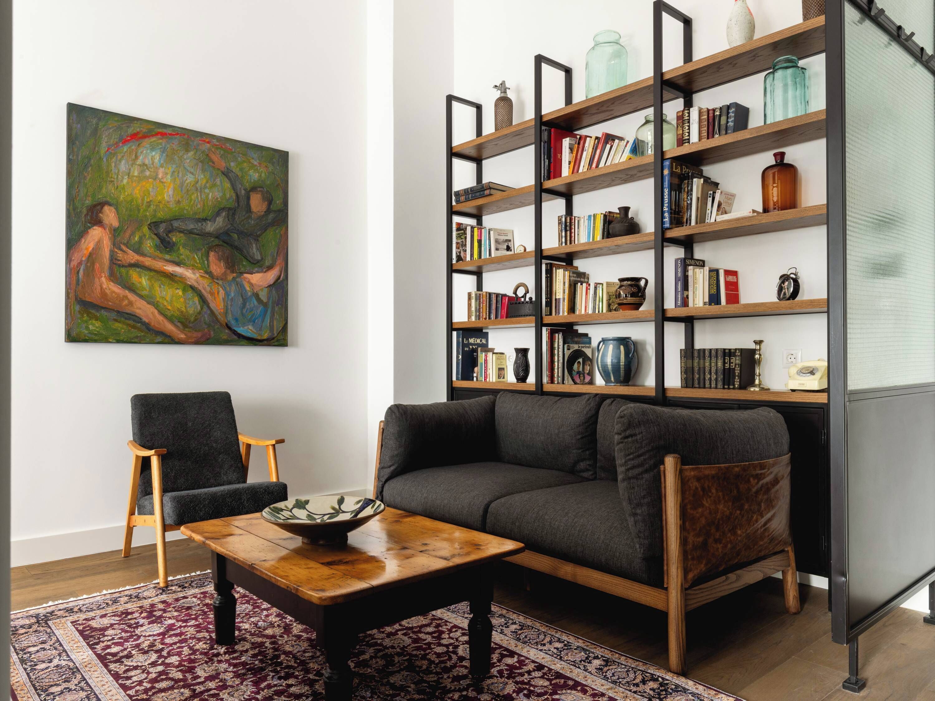 Un salon avec un canapé, une table basse, une bibliothèque et un tableau accroché au mur.