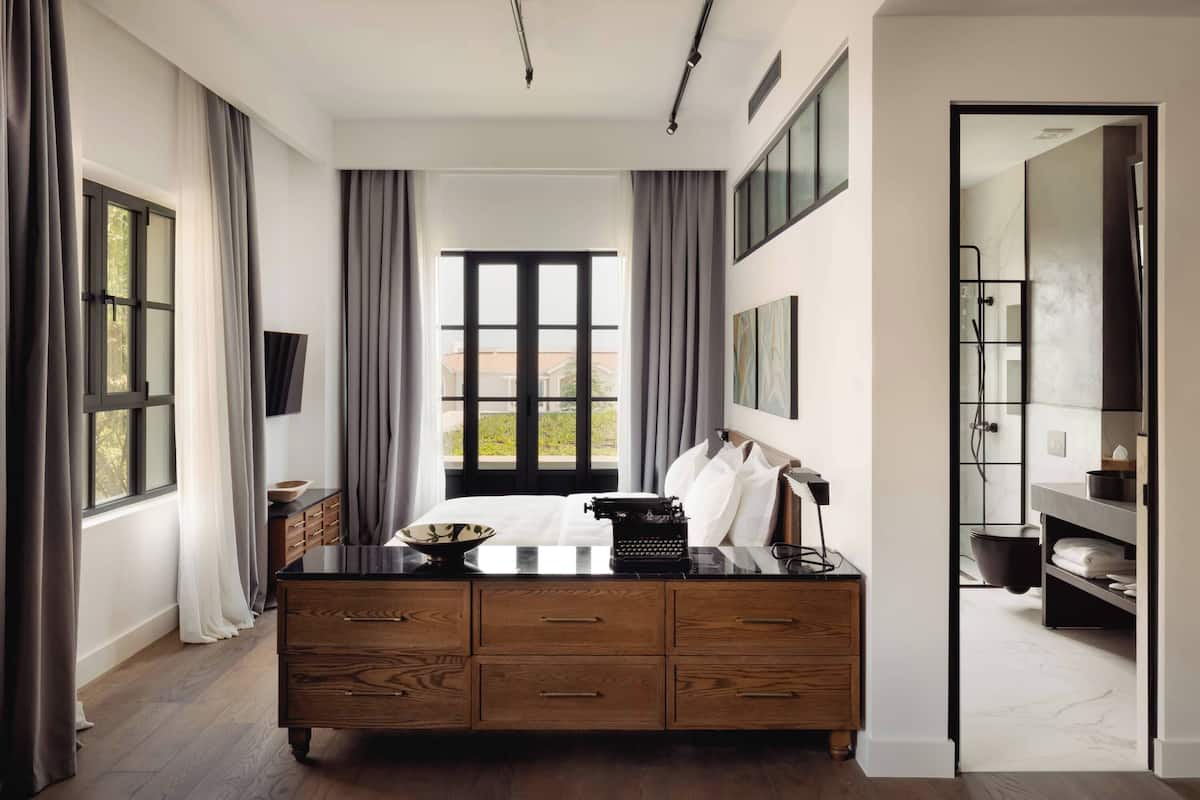 Une chambre moderne avec une commode en bois, une grande fenêtre avec des rideaux et une vue sur l’extérieur.