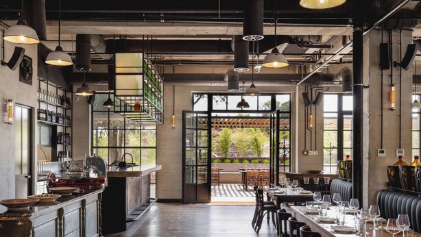 Un restaurante amplio con una larga barra de madera, varias mesas de comedor y vistas a zonas verdes.