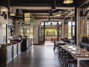 Un restaurante amplio con una larga barra de madera, varias mesas de comedor y vistas a zonas verdes.