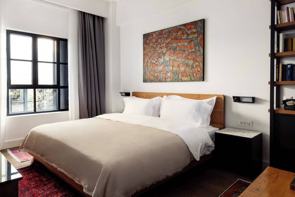 Une chambre d’hôtel moderne avec un grand lit, une table de chevet, une bibliothèque et une fenêtre avec des rideaux.