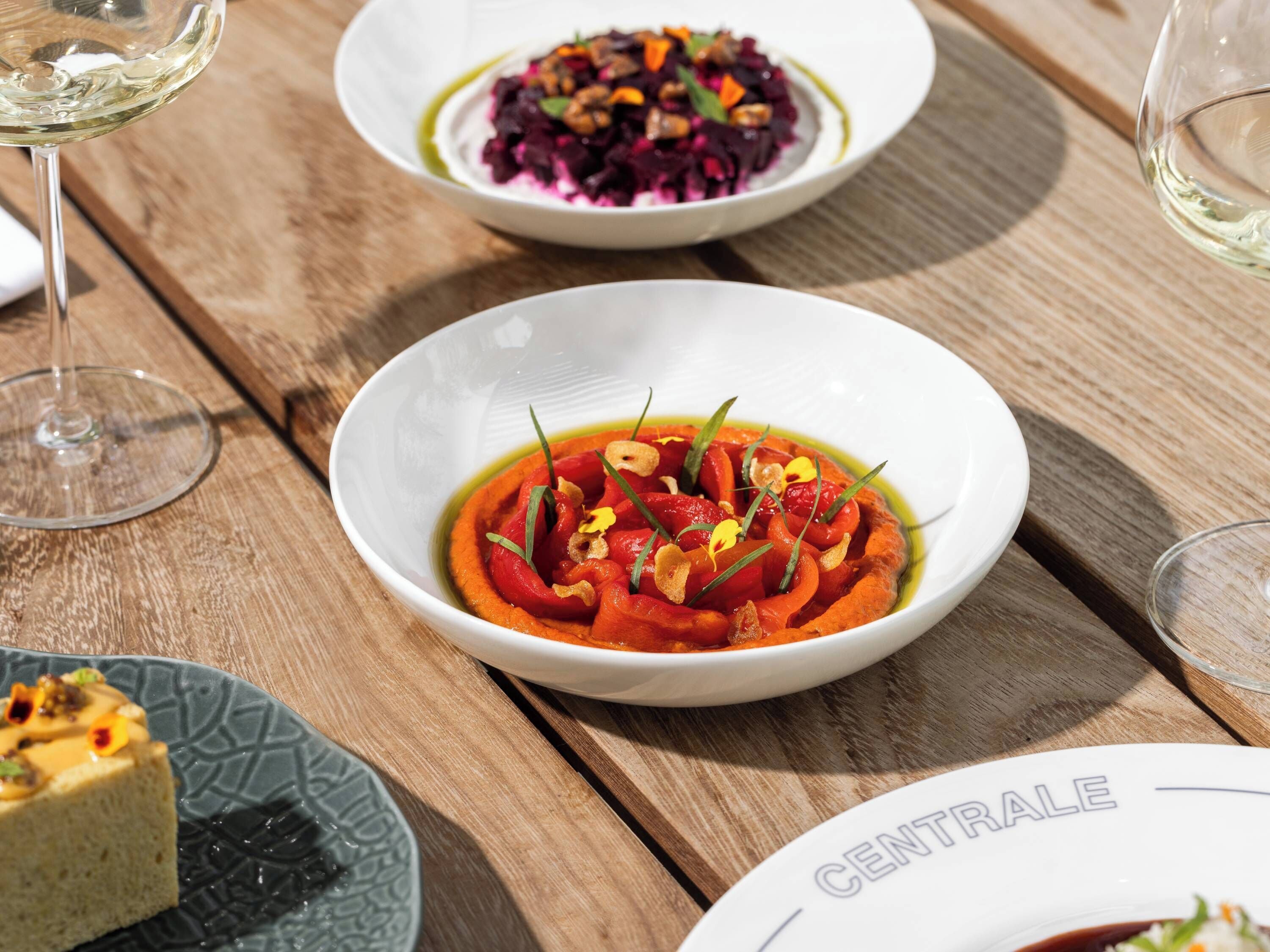 A wooden table with three dishes: a bowl of red sauce with vegetables, a bowl of purple salad, and a slice of cake.