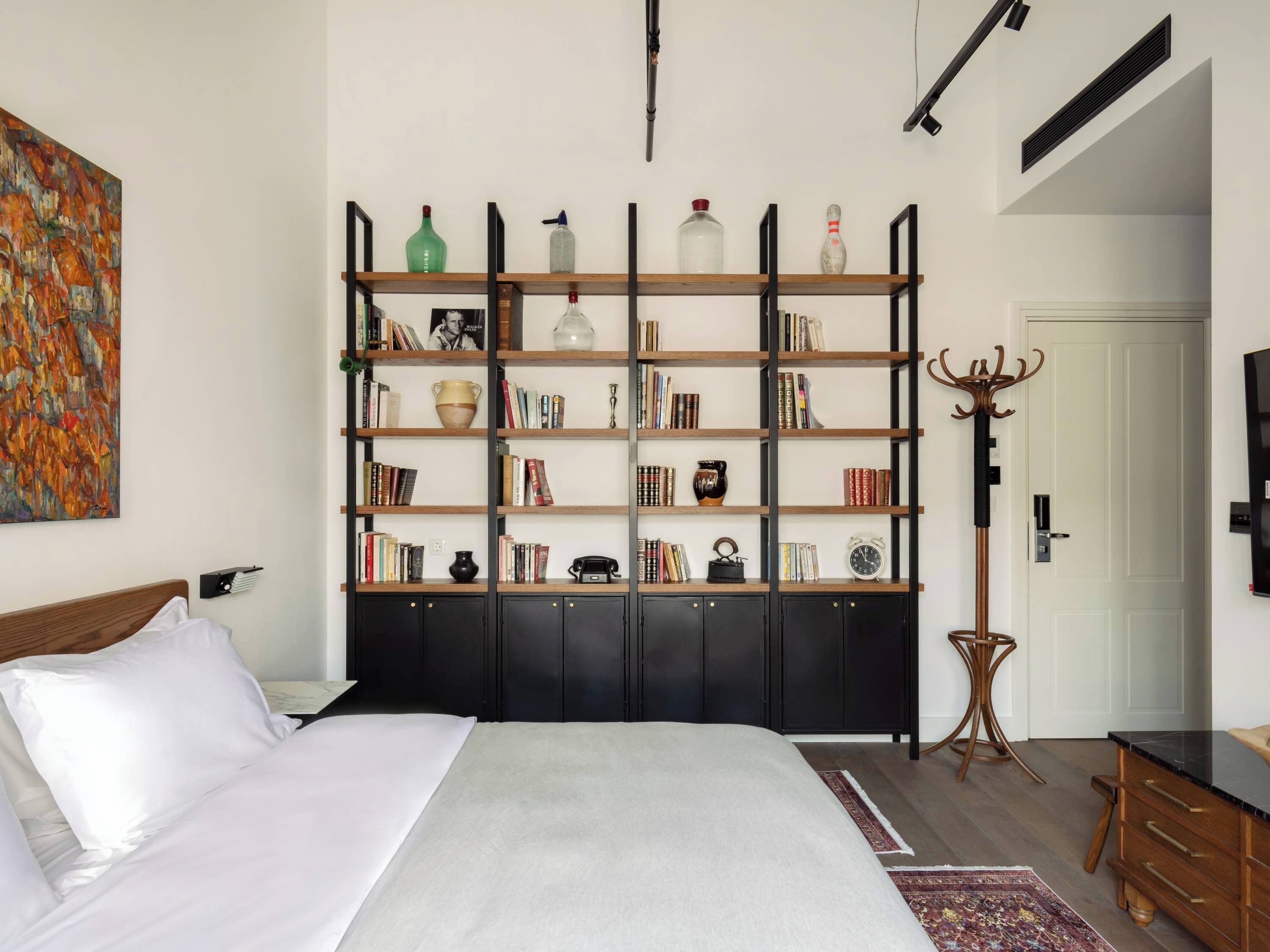 A bedroom with a large bed, a bookshelf, a coat rack, and a television.