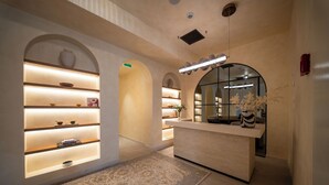 Vestíbulo de hotel con mostrador de recepción, estanterías iluminadas, alfombra estampada y un espejo grande.