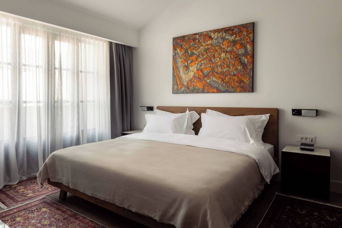 Une chambre d’hôtel avec un grand lit, une table de chevet, un tableau au mur et une fenêtre avec des rideaux.