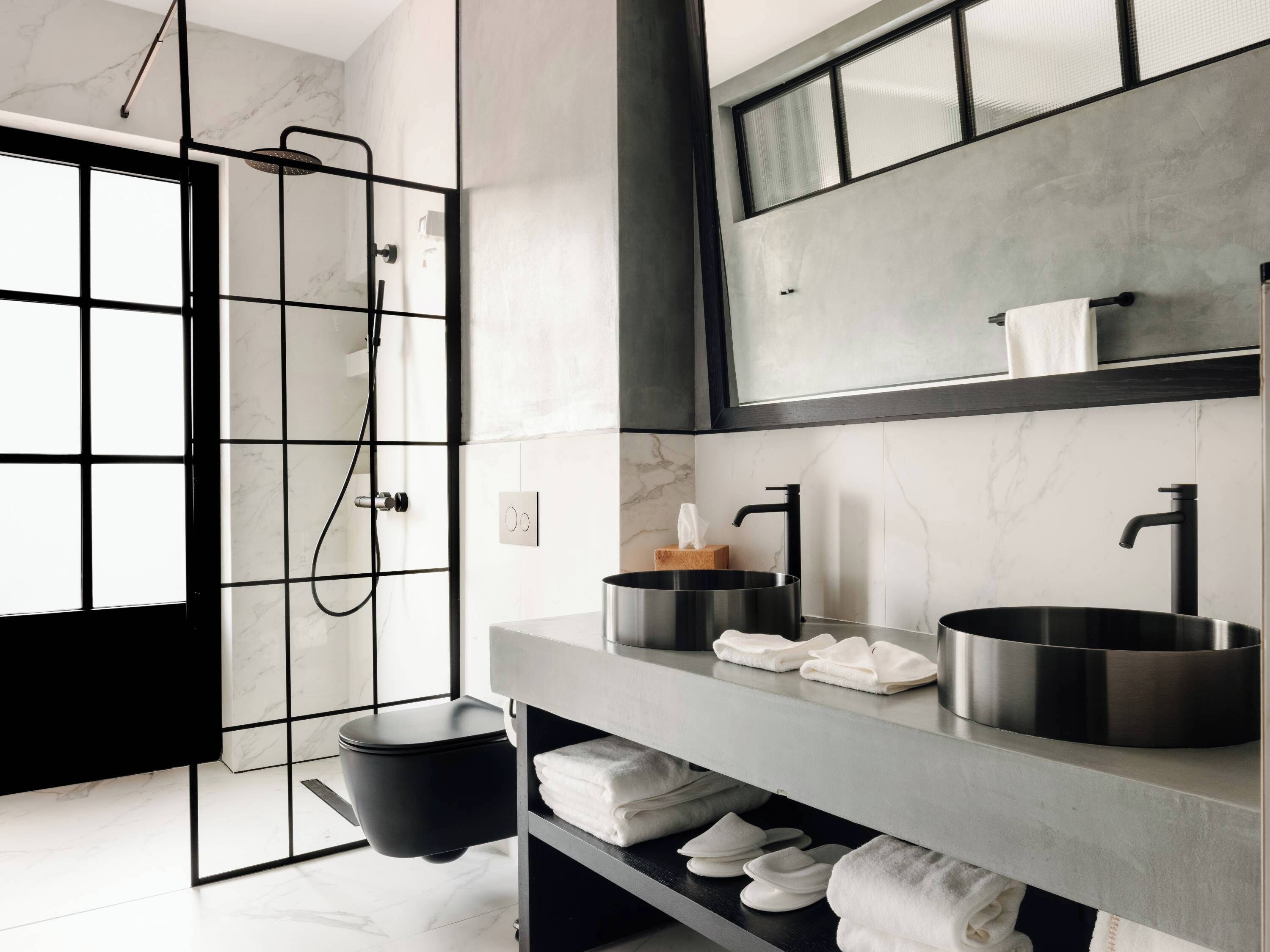A modern bathroom with a black toilet, a large mirror, and a sink with a black faucet.