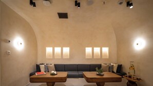 Un interior moderno con techo curvo, iluminación empotrada, un sofá modular, dos mesas de madera y un jarrón decorativo.