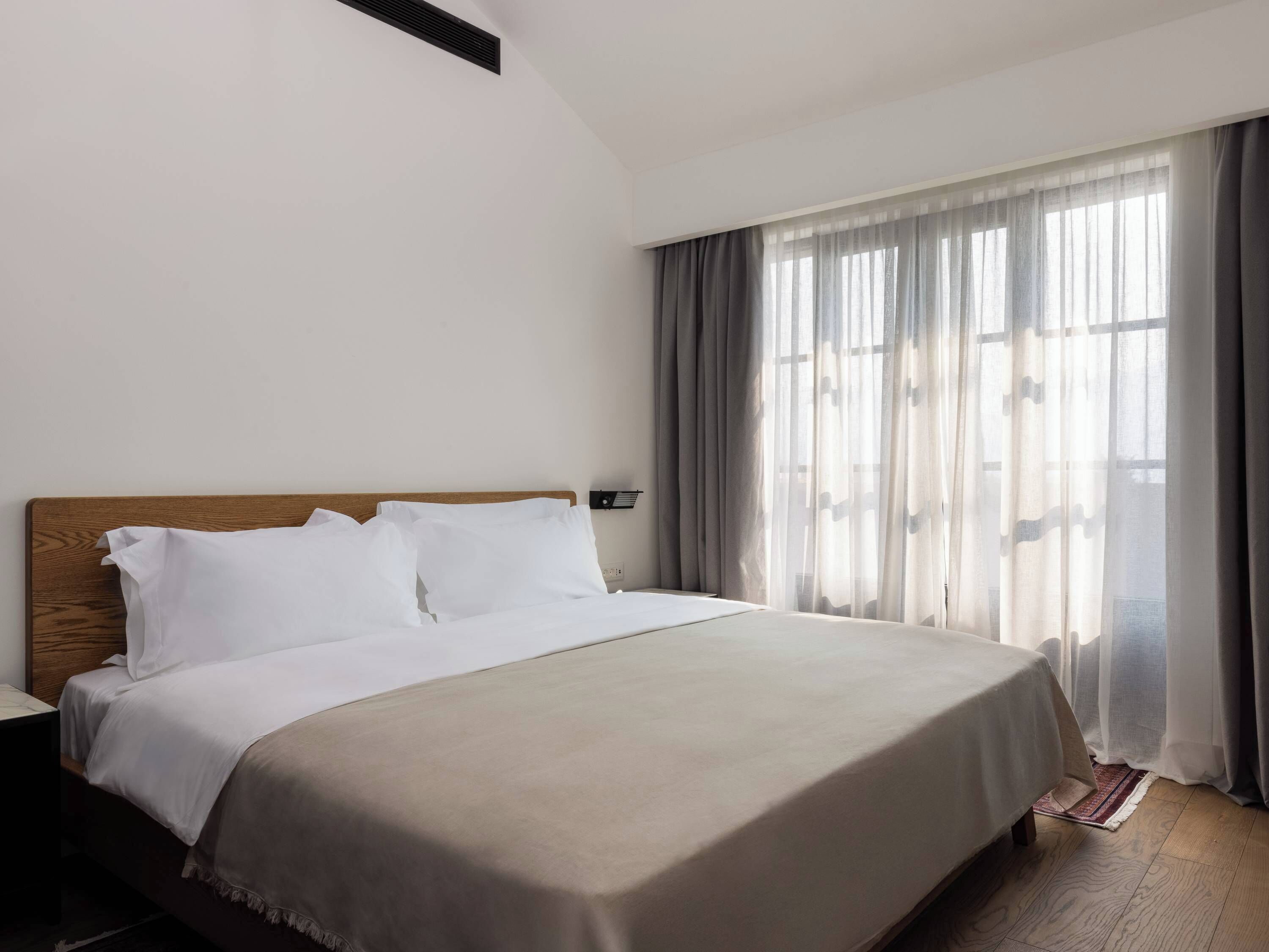Une chambre d’hôtel avec un grand lit, une tête de lit en bois et une fenêtre ornée de rideaux légers.