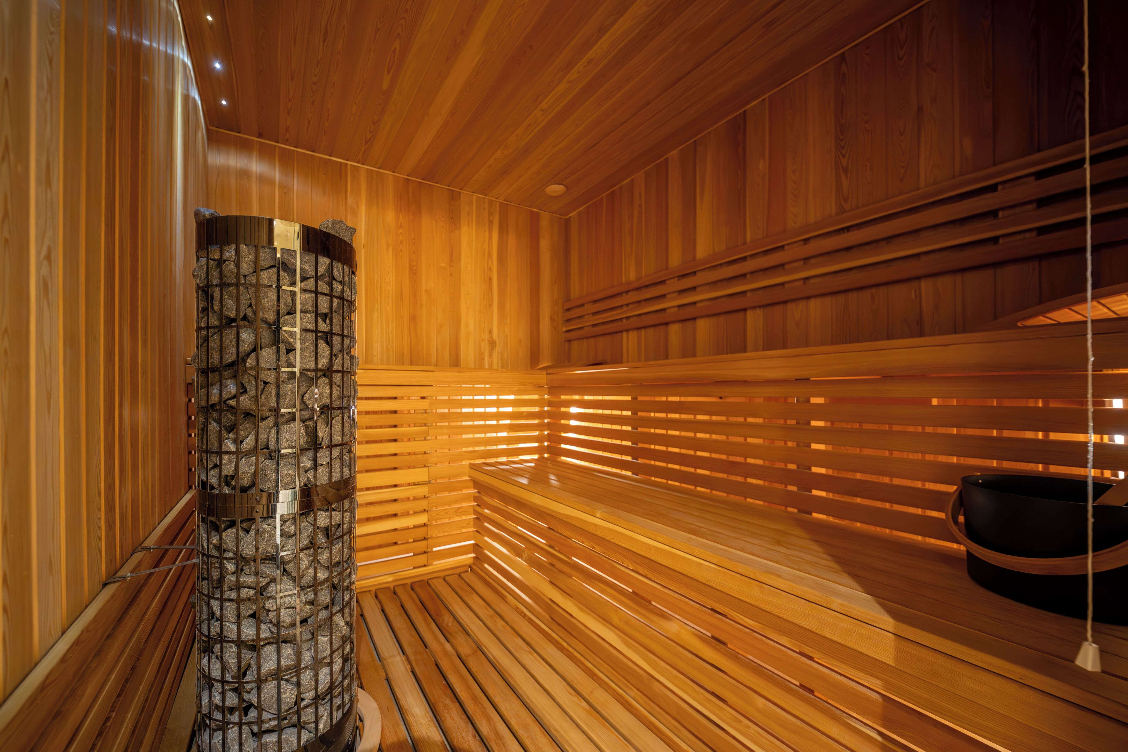 Un sauna avec des lambris en bois, un pilier en pierre et un bassin noir.