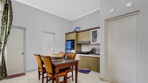 A dining area with a wooden table and chairs, a kitchen with cabinets and appliances, and a door. - OYO 94935 Rahayu Homestay (Mangunan)