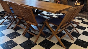 Une salle à manger avec un sol à carreaux, une table en bois et des chaises. On y trouve une cheminée avec un manteau en pierre et un lustre au-dessus.