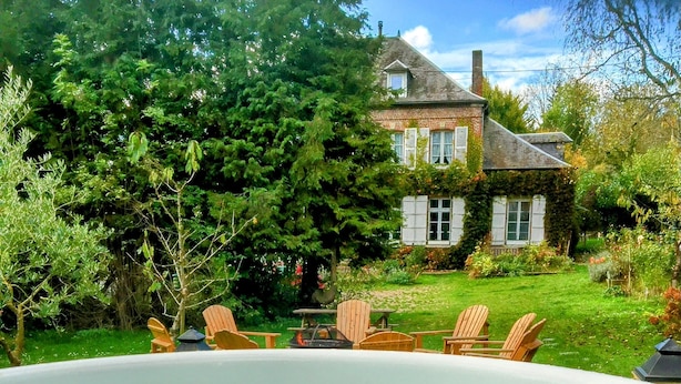 Un bain à remous entouré de meubles de jardin, avec une maison et une végétation luxuriante en arrière-plan.