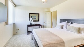 Een slaapkamer met een groot bed, een plafondventilator, een nachtkastje en een lijst met een afbeelding aan de muur.