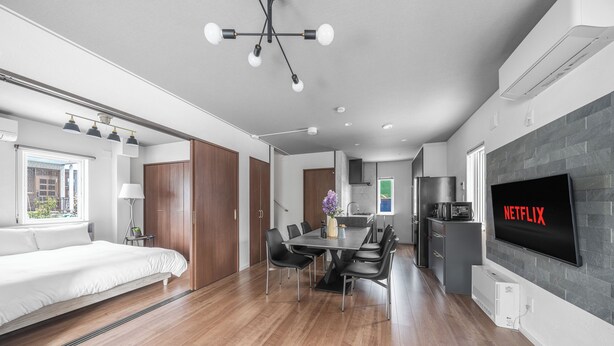 A modern, well-lit room with a dining area, a large bed, and a TV mounted on the wall. - PREGIO ASAHIKAWA (Asahikawa)