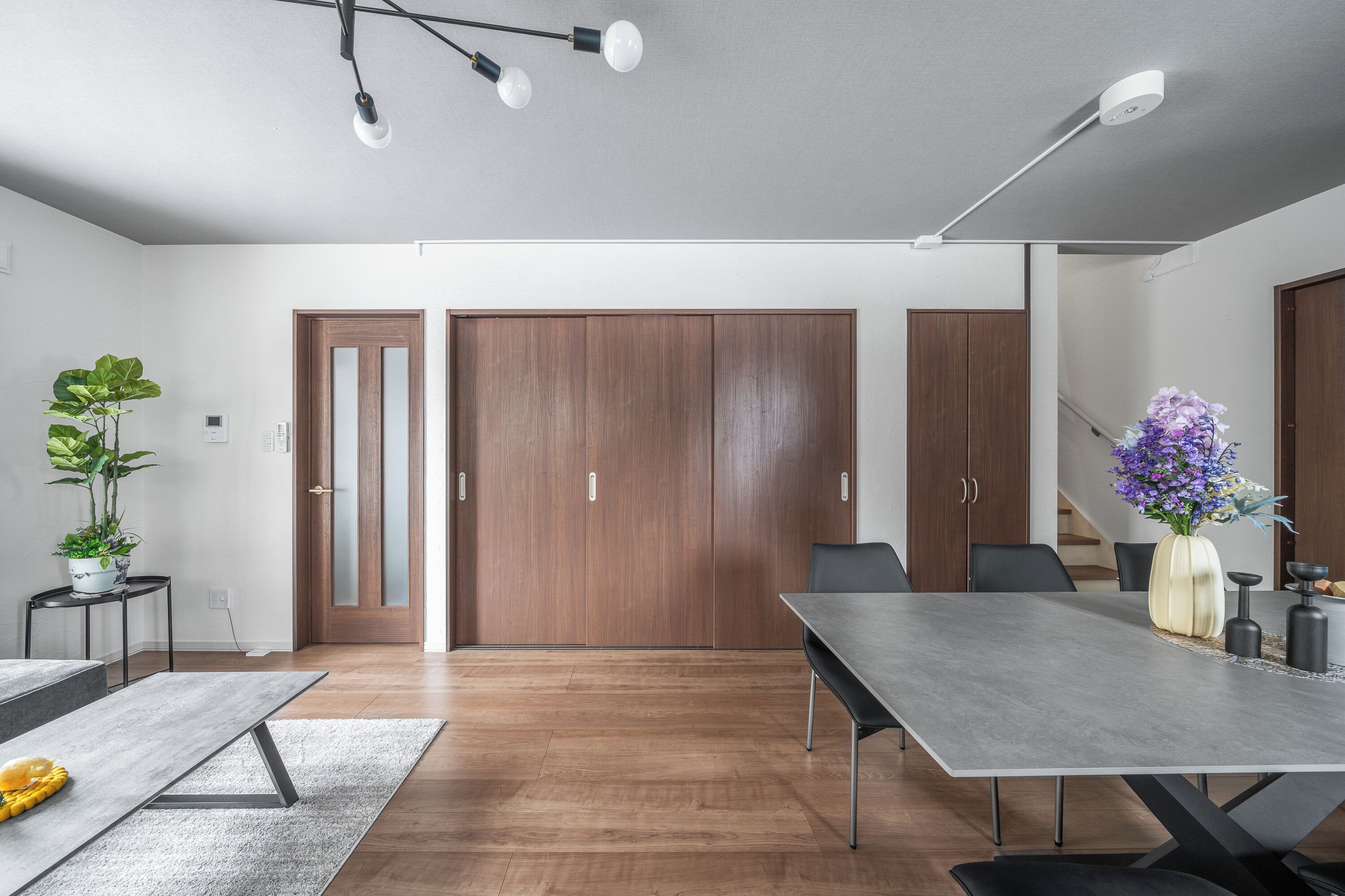 A modern conference room with a long table, wooden doors, and a potted plant.